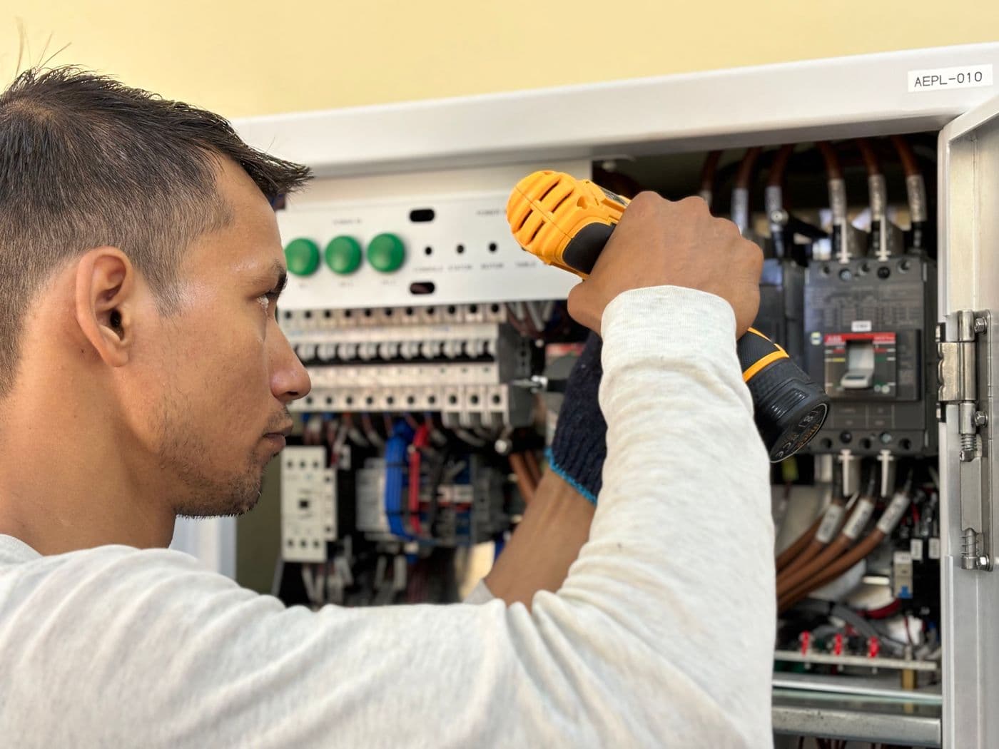 Électricien perçant une armoire électrique, disjoncteurs et câblage apparents